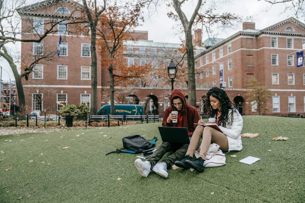 College students studying with laptops and books in a park during fall.