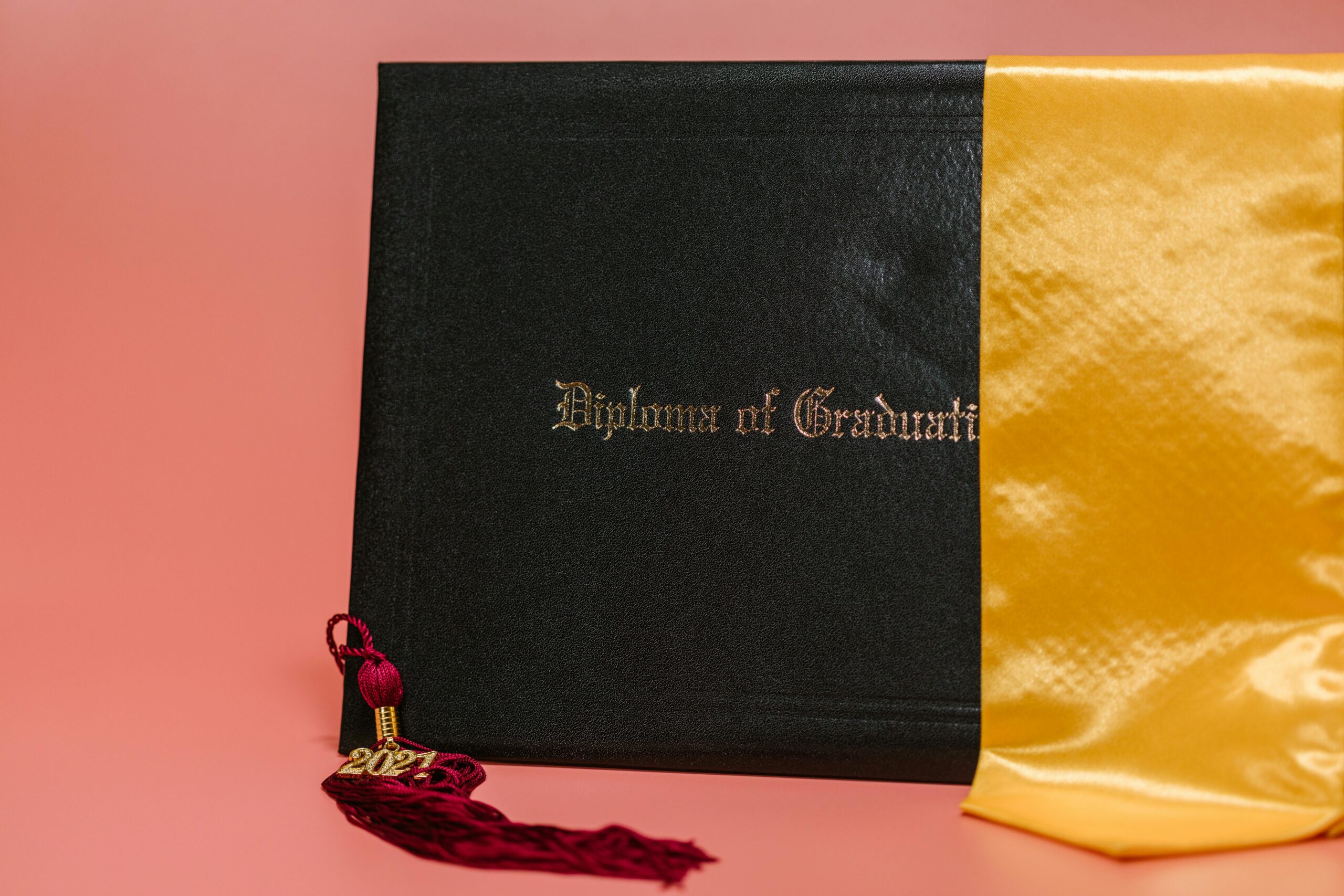 Black diploma with garnet tassel and gold sash symbolizes academic achievement.